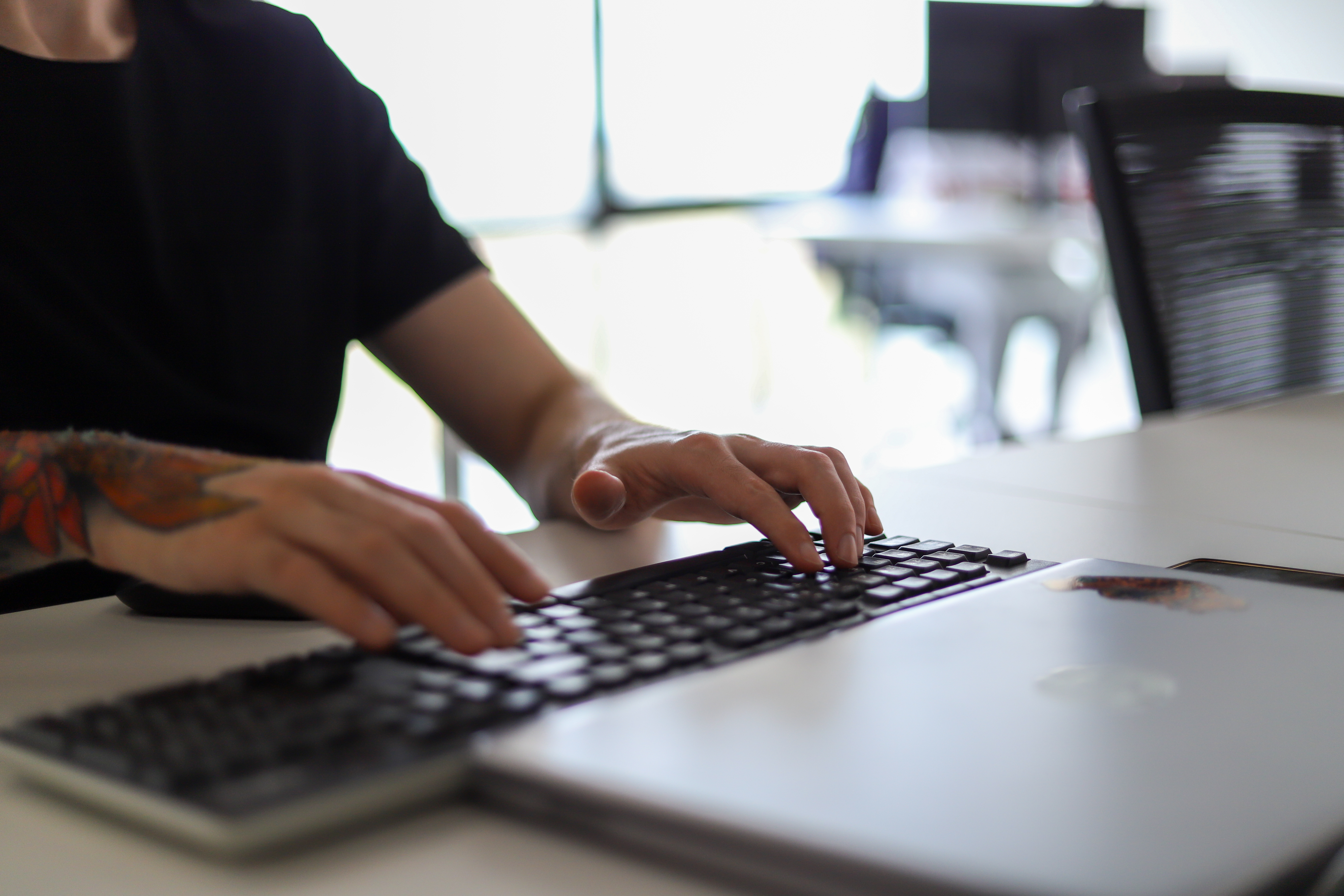 Primer plano de manos tatuadas escribiendo en un teclado